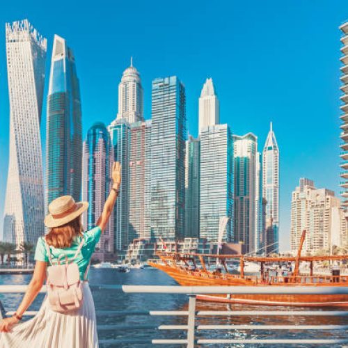 Cheerful asian traveler girl walking on a promenade in Dubai Marina district. Travel destinations and tourist lifestyle in UAE